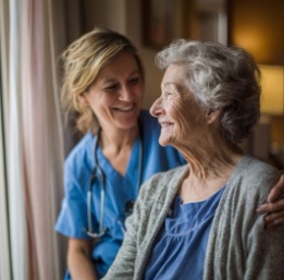 A hospice caregiver smiles while sitting beside an elderly woman near a window, offering comfort and reassurance. This warm moment reflects compassionate hospice care in Winfield, KS, focused on dignity and supportive guidance.
